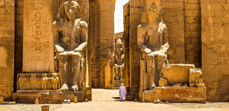 Un uomo cammina nel Tempio di Luxor con due grandi statue ai lati