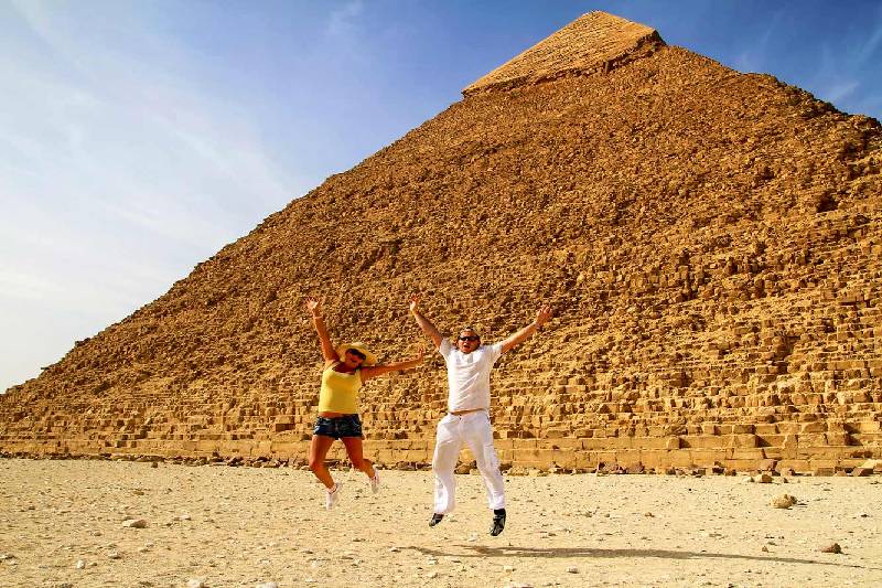 una donna e un uomo saltano con la piramide dietro di loro